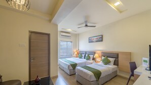 A hotel room with two beds, a desk, a chair, a ceiling fan, and a painting on the wall. - Treebo Nestlay Airport Alandur (Chennai)