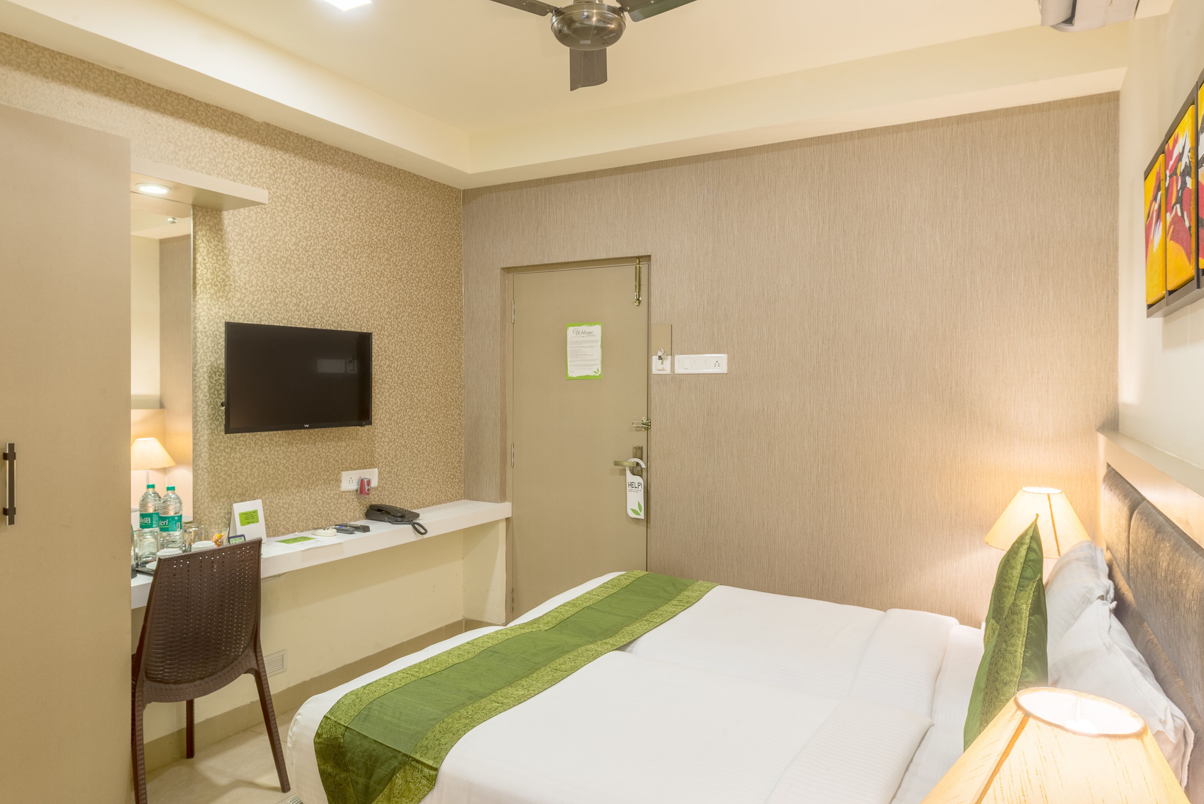 A hotel room with a bed, a desk, a chair, a television, and a door.