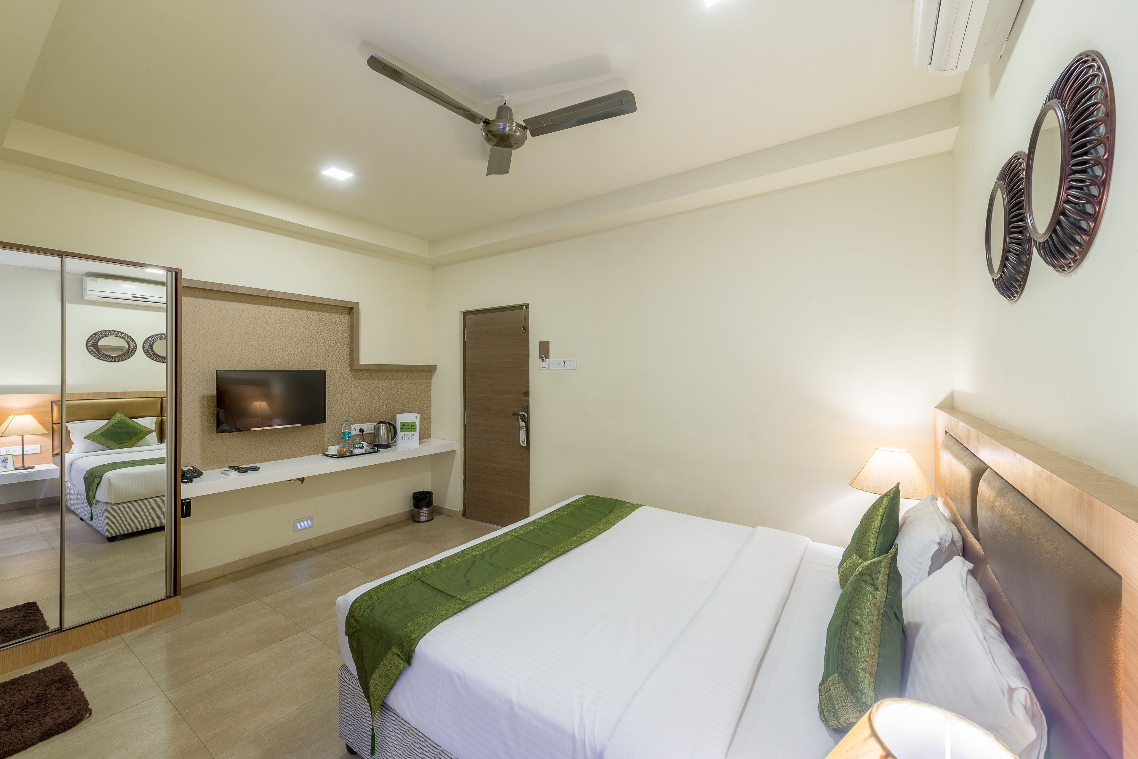 A hotel room with a bed, a TV, a ceiling fan, and a mirror on the wall.