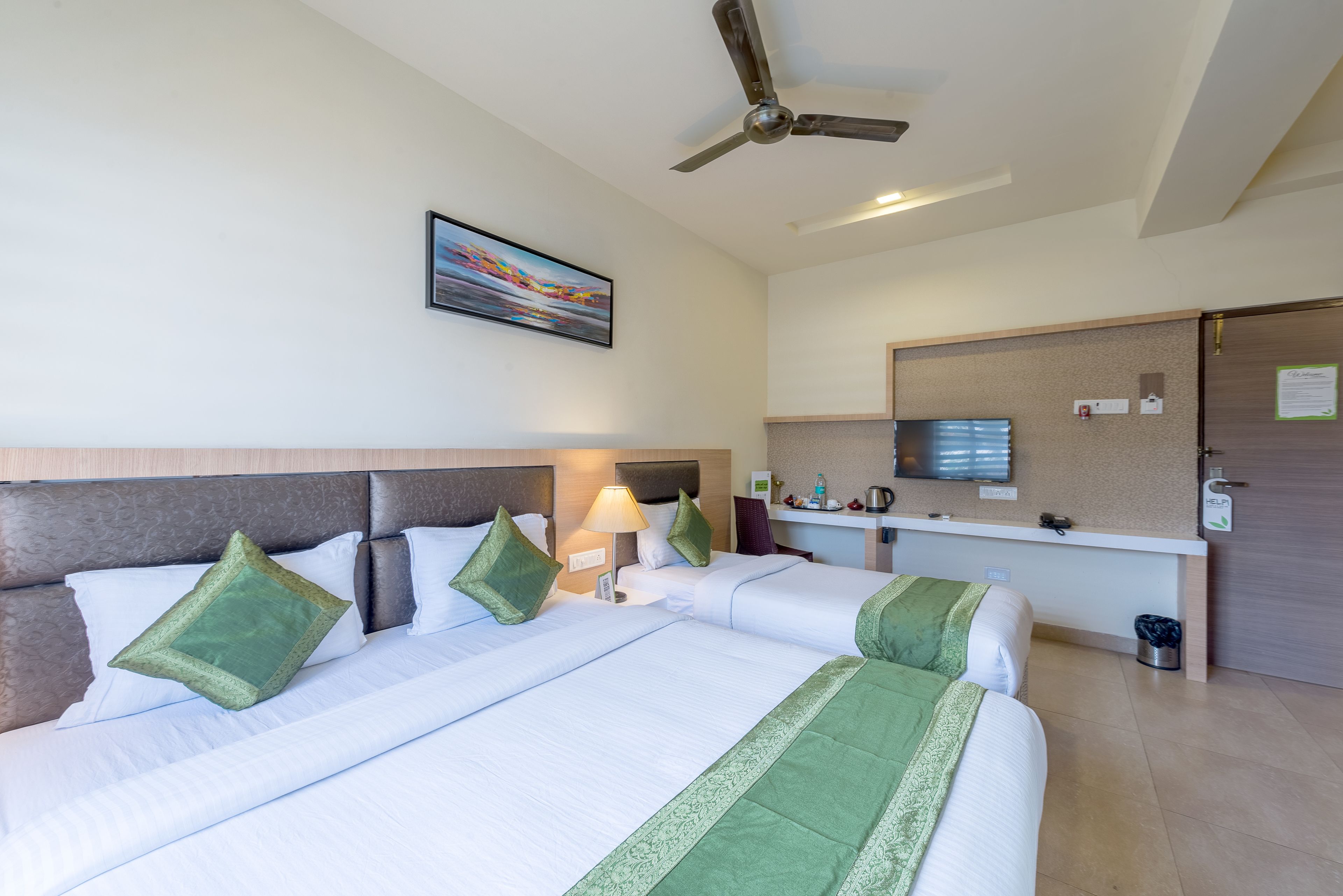 A hotel room with two beds, a ceiling fan, a painting, a desk with a computer, and a small trash bin.