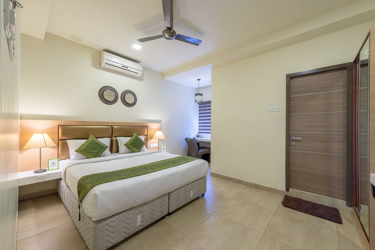 Ein Hotelzimmer mit einem Bett, Nachttischlampen, einer Klimaanlage, einem Deckenventilator, einem Schreibtisch und einer Tür.