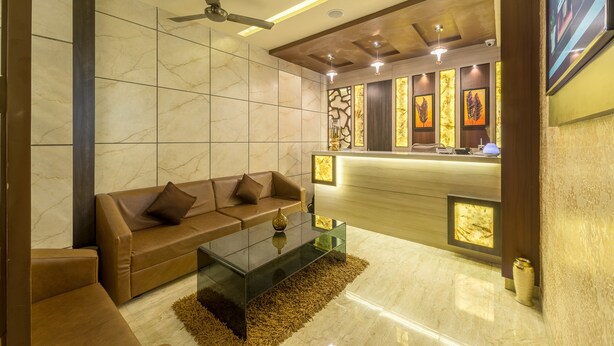 A modern lobby with a brown leather sofa, a glass coffee table, and a reception desk with framed artwork. - Treebo Nestlay Airport Alandur (Chennai)