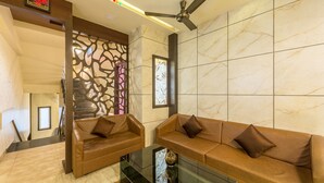 A modern living room with two leather sofas, a glass coffee table, and a ceiling fan. - Treebo Nestlay Airport Alandur (Chennai)