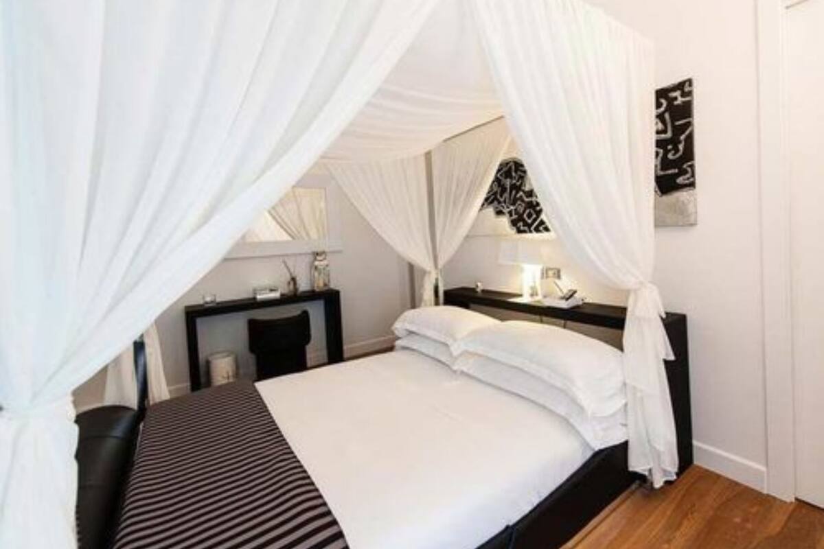 A bedroom with a canopy bed, a bedside table, a lamp, and a wall art piece.