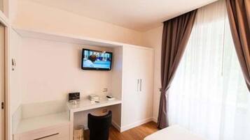 A hotel room with a bed, a TV mounted on the wall, a small desk with a chair, and a window with curtains.