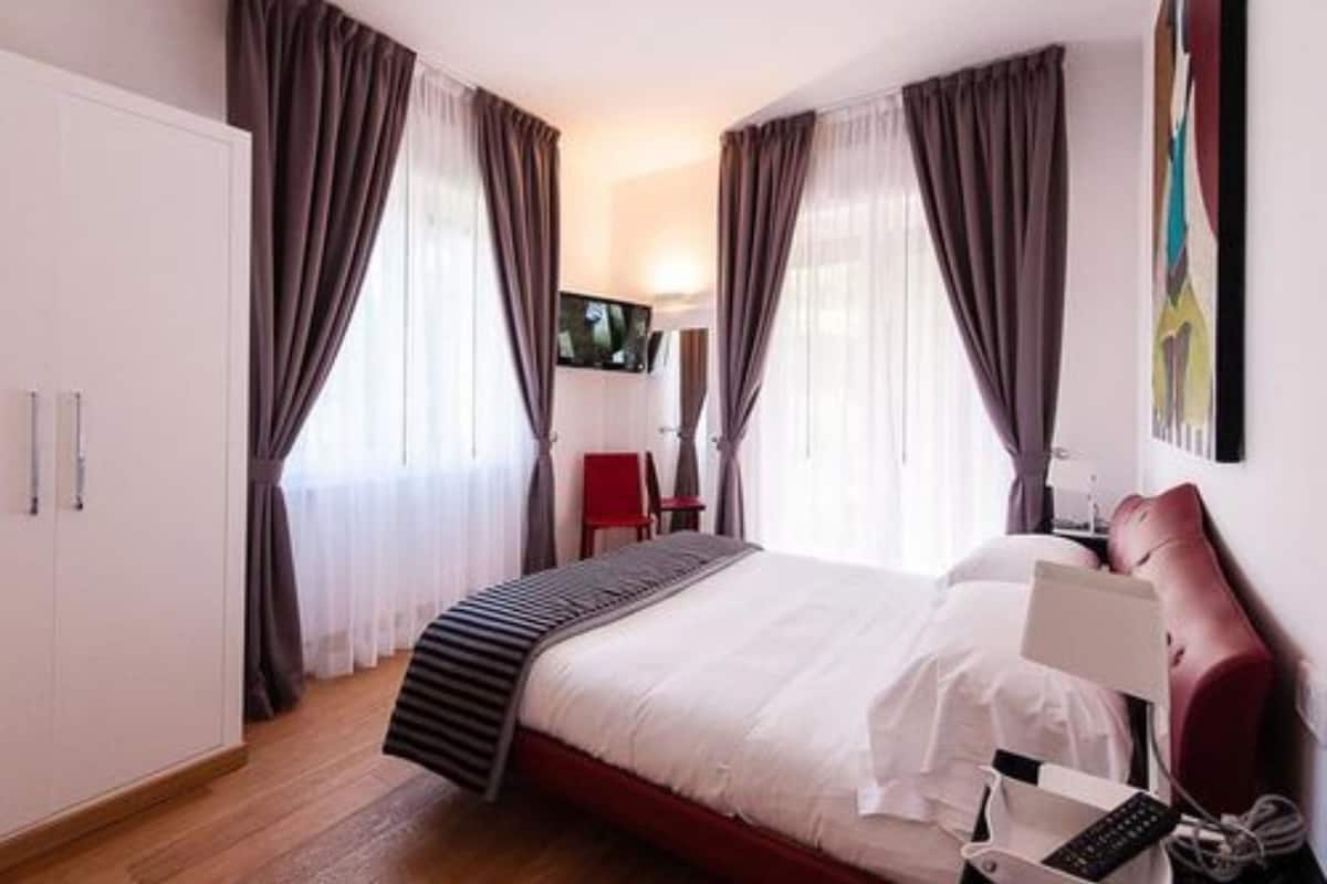 A hotel room with a bed, a TV mounted on the wall, a desk with a chair, and a wardrobe.