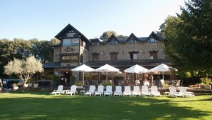 A hotel with a stone facade, outdoor seating area with white chairs and umbrellas, and a well-maintained lawn. - Florido Hotel (Sort)