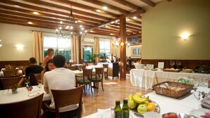 A restaurant with wooden beams, tables with white tablecloths, and a buffet area with fruits and bread baskets. - Florido Hotel (Sort)