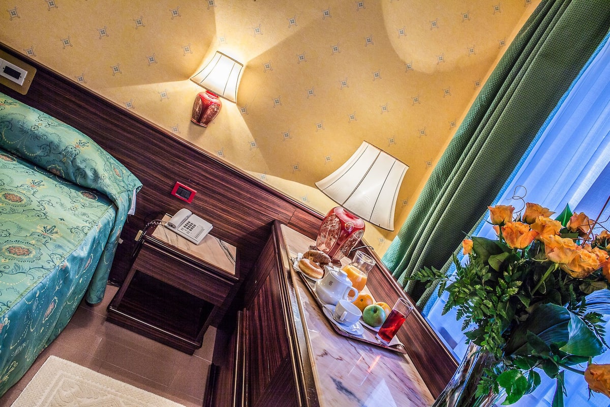 Ein Hotelzimmer mit einem Bett, einem Nachttisch mit Lampe, einem Telefon und einem Tablett mit Frühstücksgegenständen.