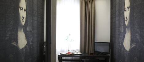 A hotel room with a bed, a desk, a television, and a window with curtains.