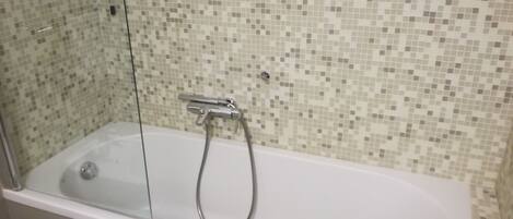 Un baño con una bañera blanca, cabina de ducha de vidrio y pared revestida con mosaicos.