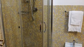 A glass-enclosed shower with a handheld showerhead and a wall-mounted faucet.