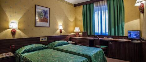 Habitación de hotel con dos camas, un escritorio, una silla, un televisor y una ventana con cortinas verdes.