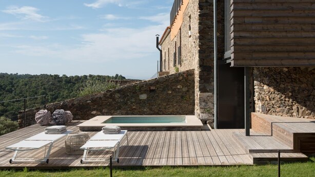 A pool area with lounge chairs and a stone wall. - Mas Vivent (Vilamaniscle)