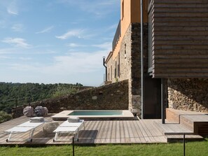 A pool area with lounge chairs and a stone wall. - Mas Vivent (Vilamaniscle)