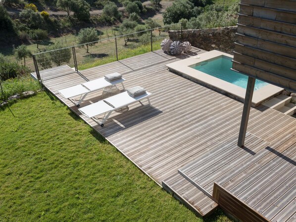 Une terrasse en bois avec une piscine, des chaises longues et un mur en pierre.