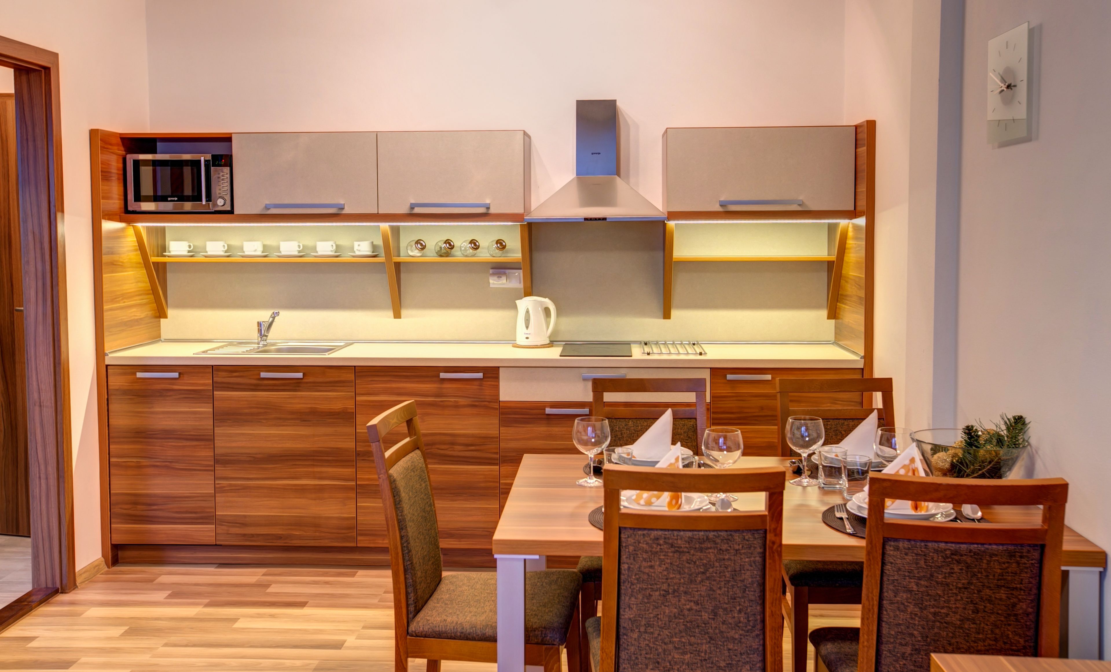 A modern kitchen with wooden cabinets, a microwave, and a dining area with chairs and a table set for two.