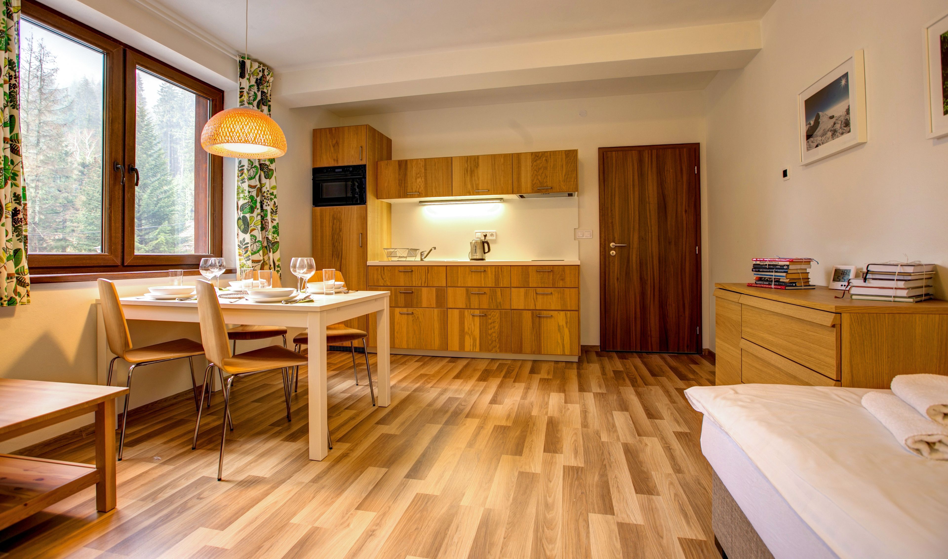A compact kitchen with wooden cabinets, a dining area with a table set for two, and a bed with a neatly made bed.