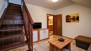 A staircase leading to a room with a television, wooden cabinets, a table with a decorative item, and a painting on the wall. - Apartmány TRI STUDNIČKY (Demanovska Dolina)