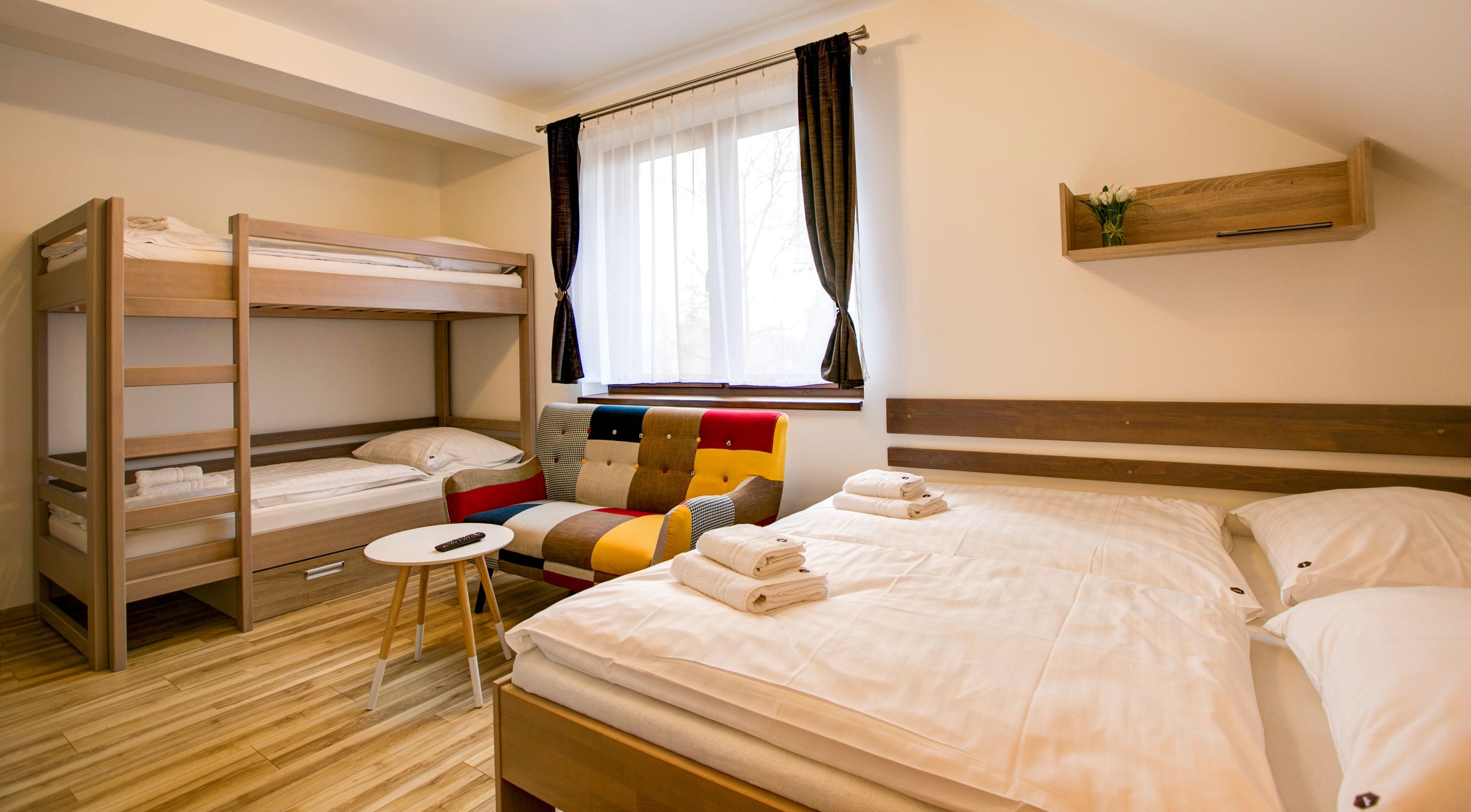 Una habitación con literas, una cama individual, una mesa redonda pequeña y una ventana con cortinas.