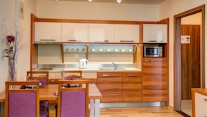 A modern kitchen with wooden cabinets, a built-in microwave, and a dining area with purple chairs. - Apartmány TRI STUDNIČKY (Demanovska Dolina)