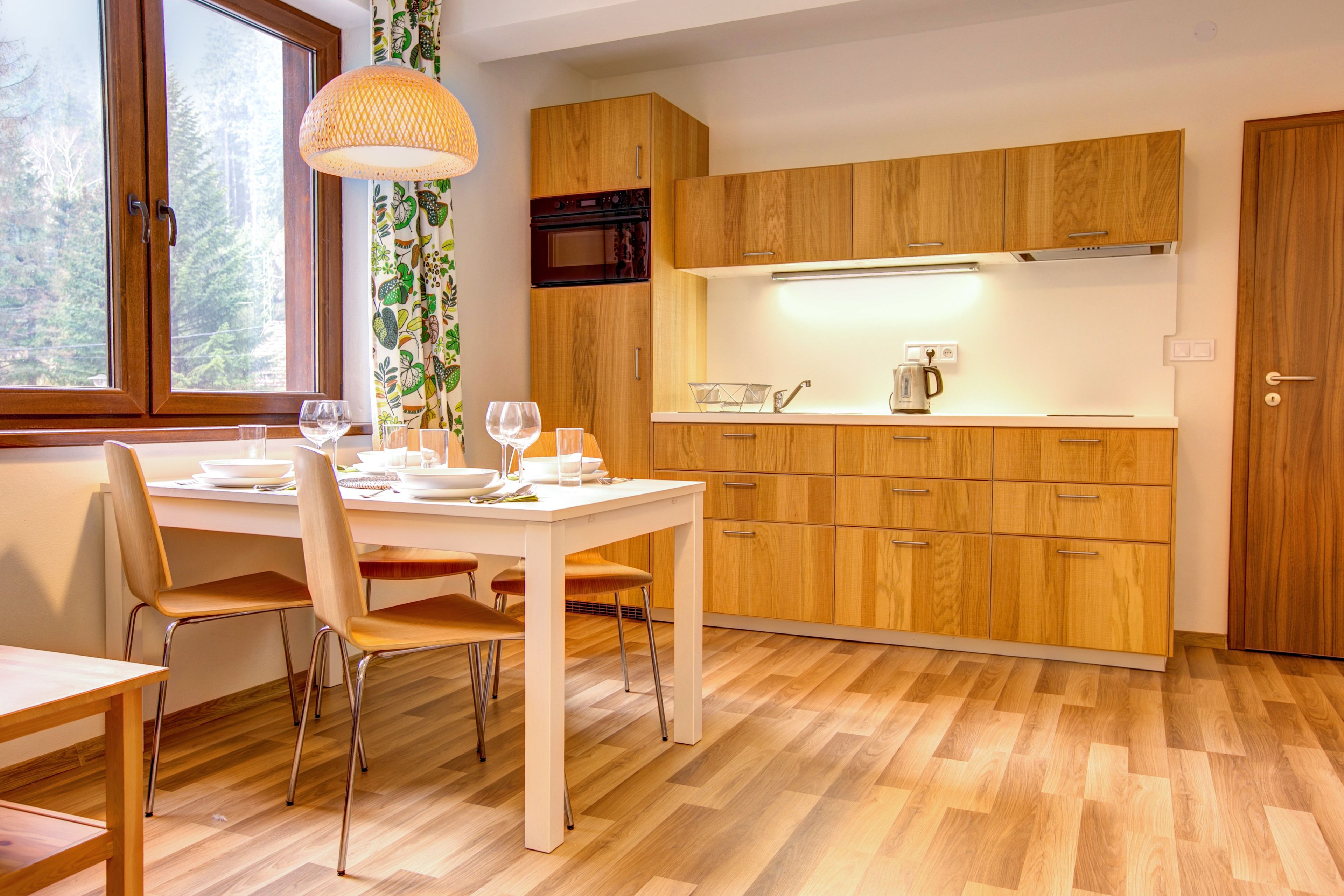 A modern kitchen with wooden cabinets, a white countertop, and a dining area with a table and chairs.