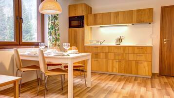 A modern kitchen with wooden cabinets, a white countertop, and a dining area with a table and chairs.