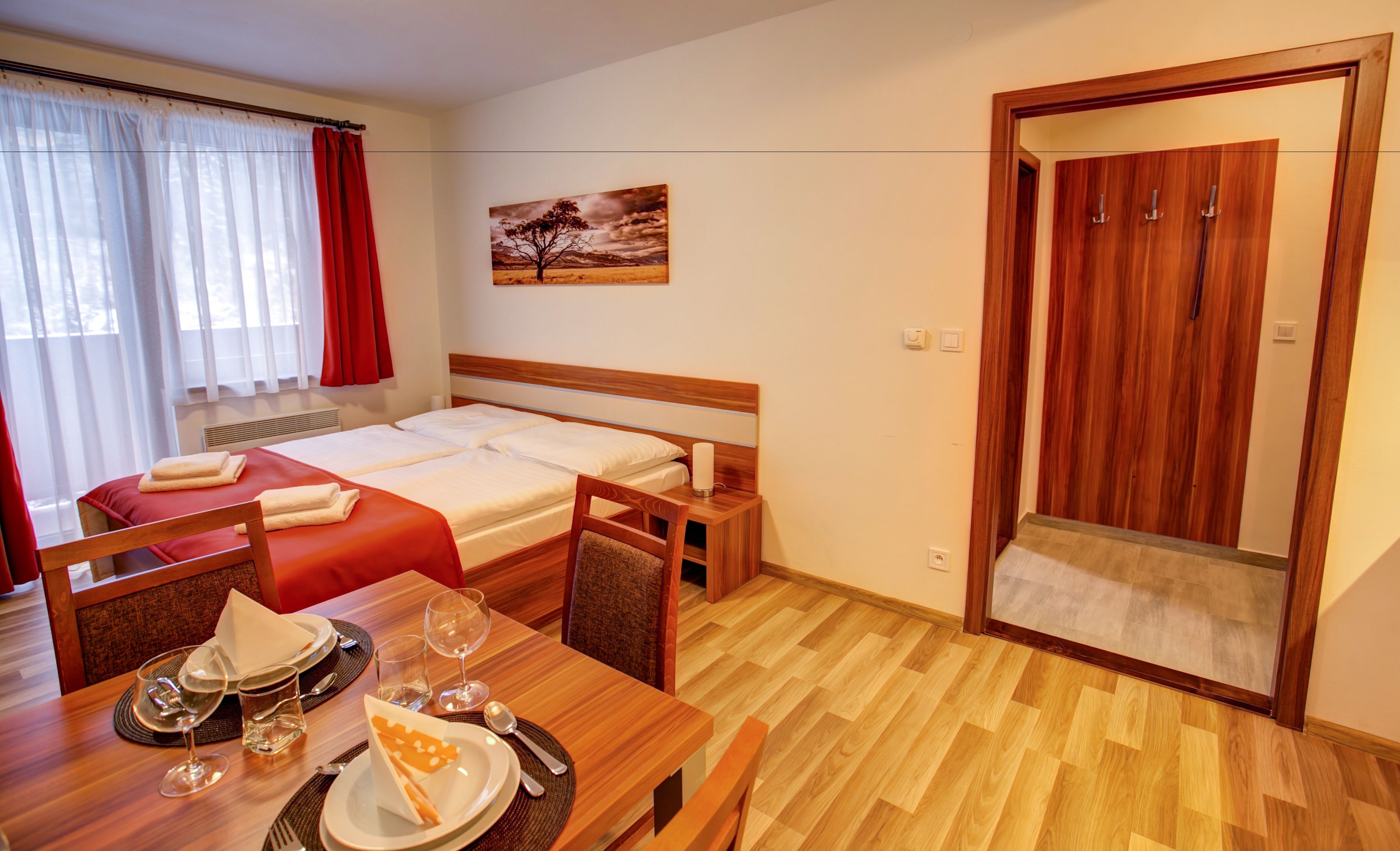 A hotel room with a bed, a dining table with chairs, a painting on the wall, and a wooden wardrobe.