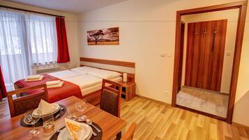 A hotel room with a bed, a dining table with chairs, a painting on the wall, and a wooden wardrobe.