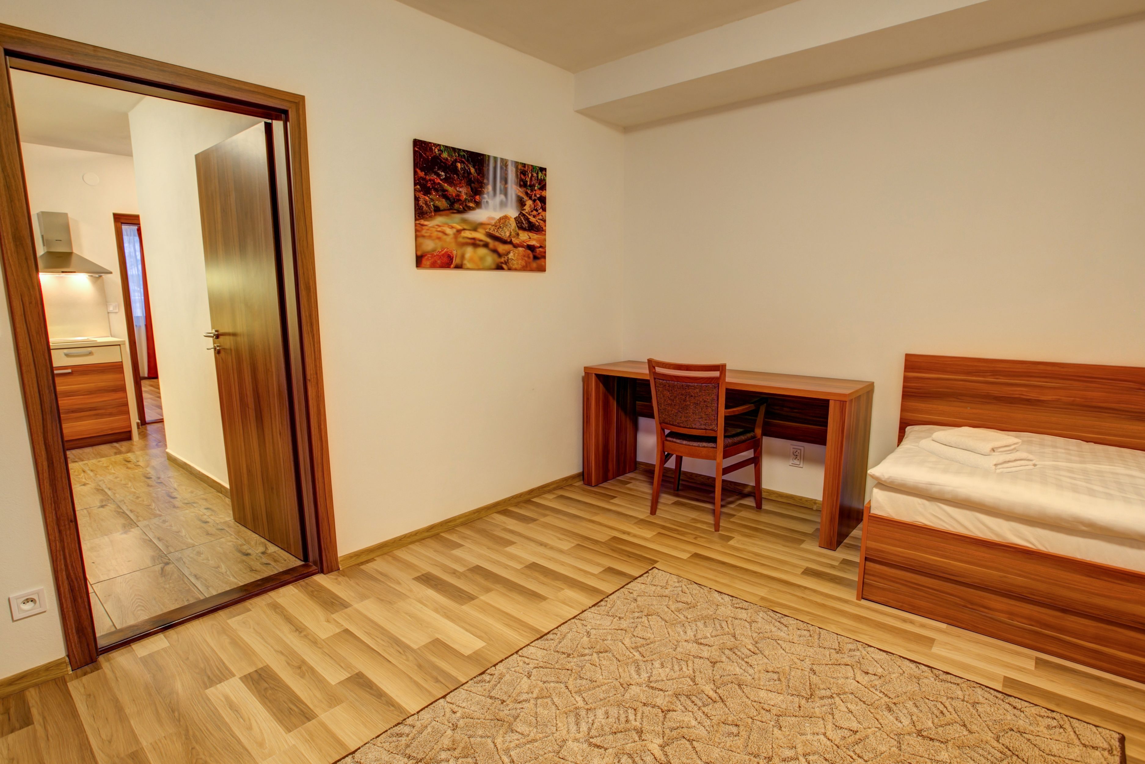 A bedroom with a wooden bed, a desk with a chair, a mirror, and a painting on the wall.