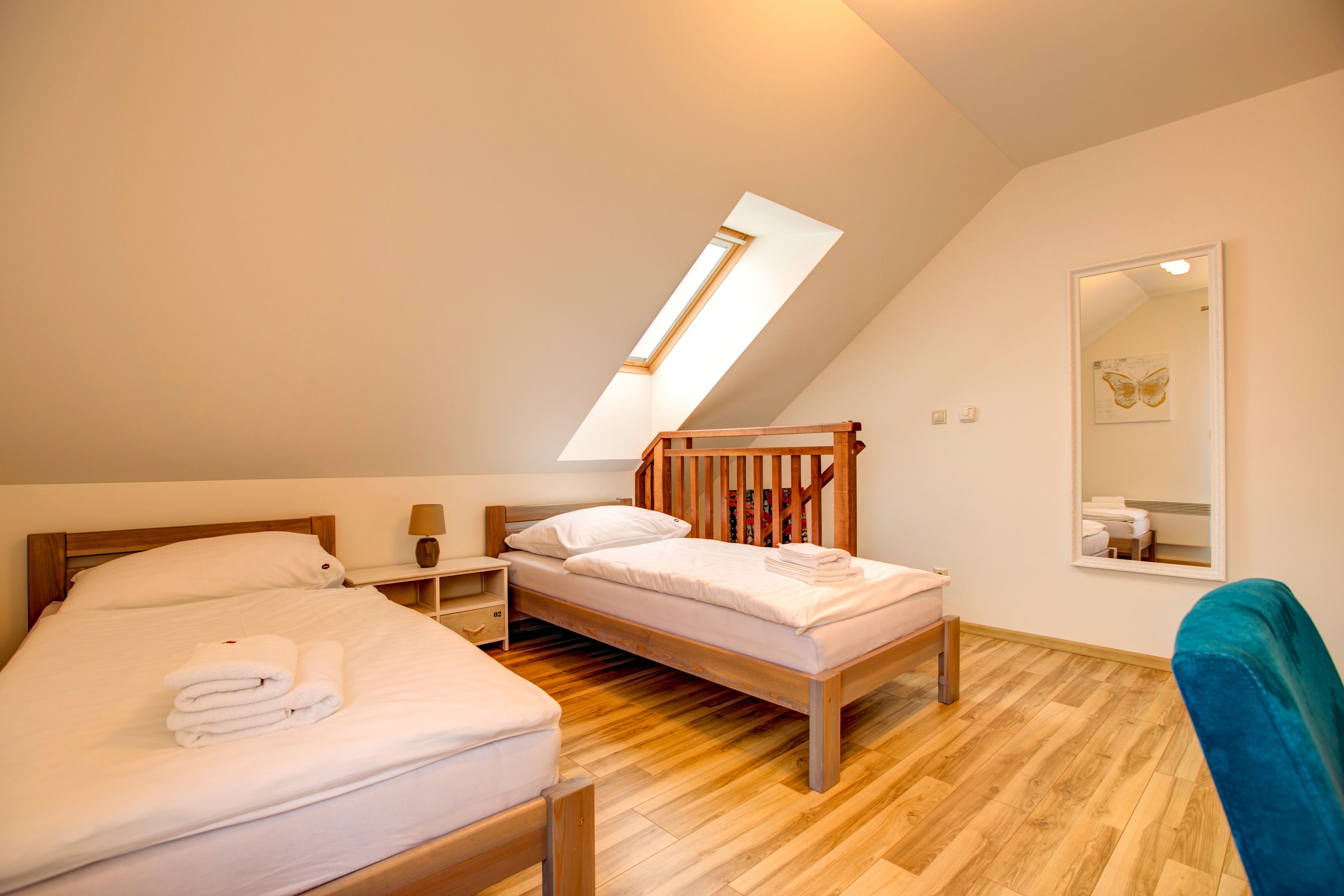 A bedroom with two beds, a skylight, a mirror, and a wooden floor.