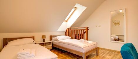 A bedroom with two beds, a skylight, a mirror, and a wooden floor.