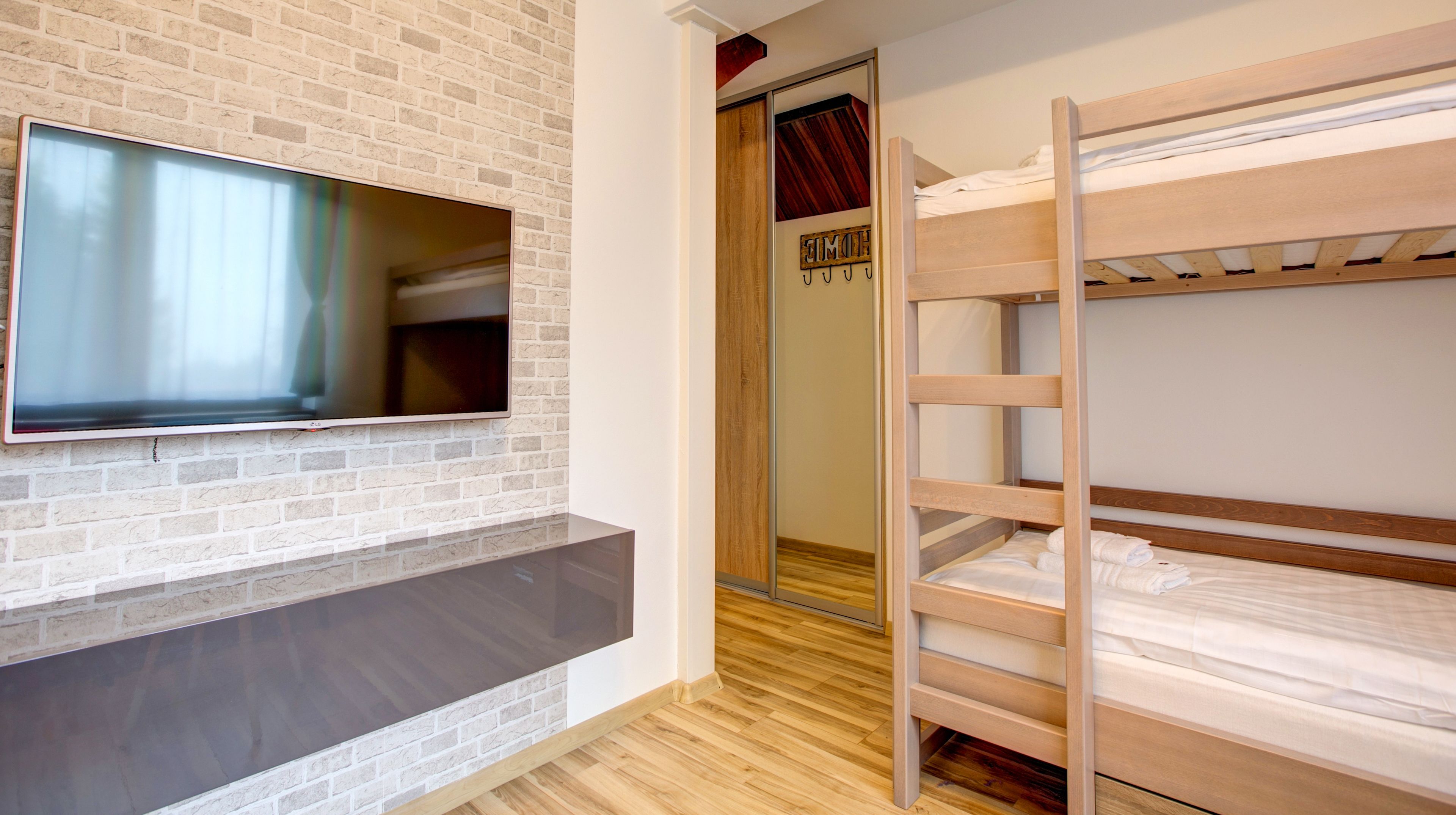 Una habitación con un televisor montado en una pared de ladrillo, una cama litera y una puerta de madera con una placa identificativa.