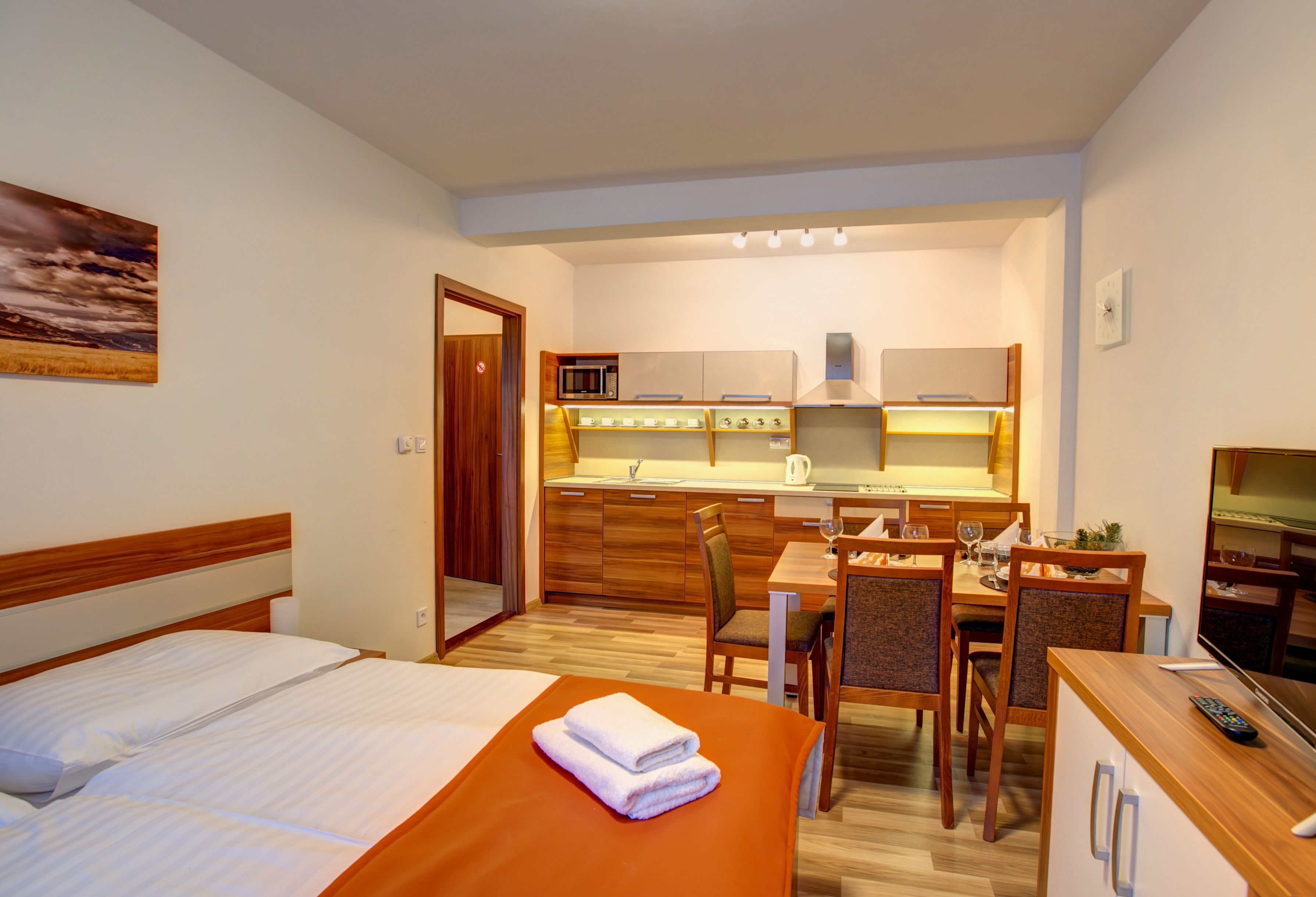 A hotel room with a bed, a dining table with chairs, a kitchen area with a microwave, and a TV.