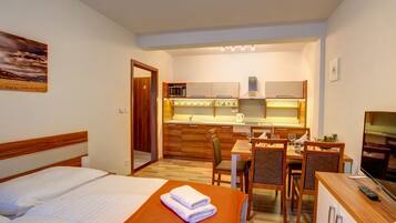 A hotel room with a bed, a dining table with chairs, a kitchen area with a microwave, and a TV.