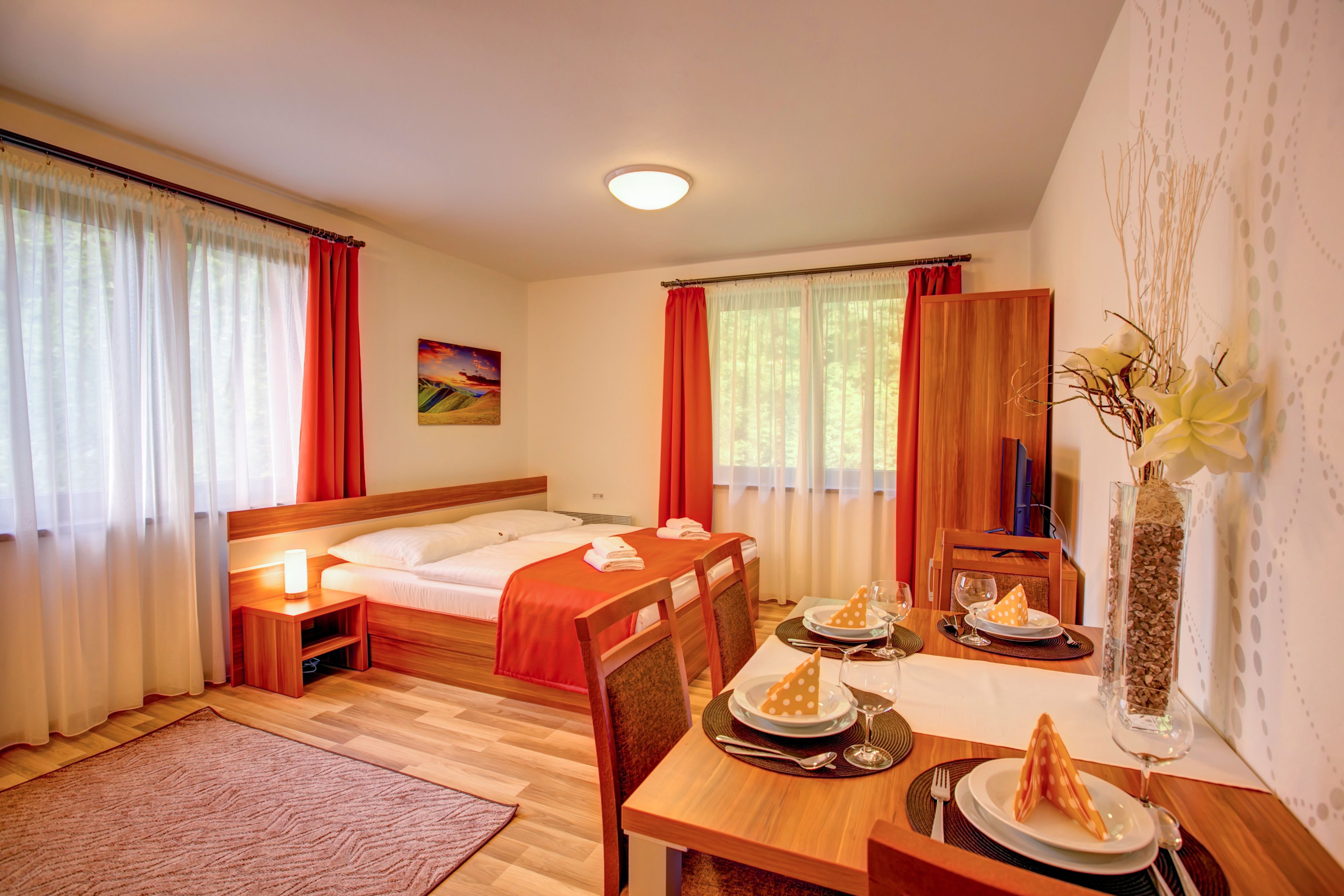 Ett hotellrum med en säng, ett matbord dukat för två personer och en vas med grenar.