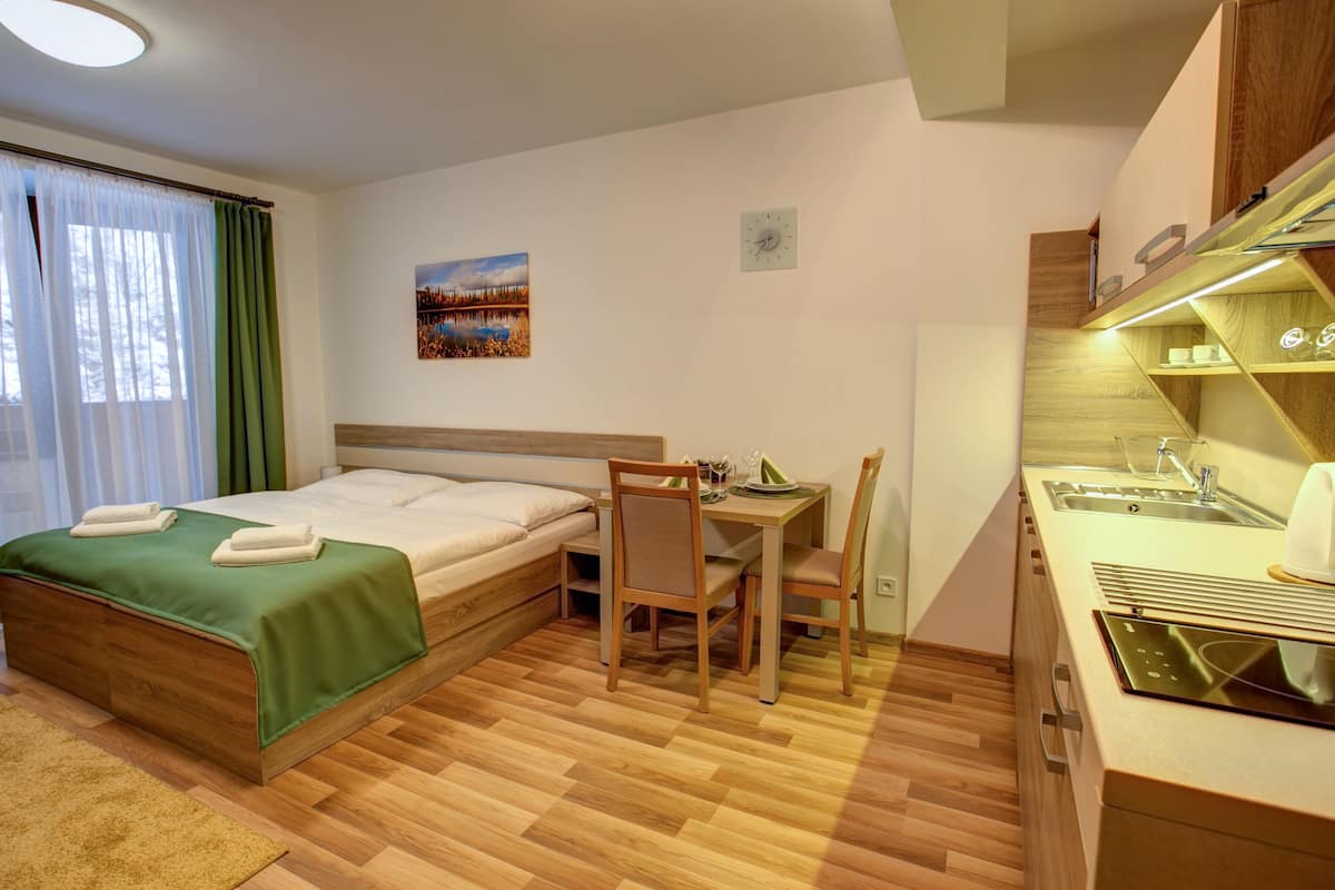 Ein Hotelzimmer mit Bett, Schreibtisch, Stuhl, einer kleinen Küche und einem Fenster mit Vorhängen.