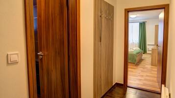 A hallway with wooden doors, a bed with green curtains, and a wooden floor.
