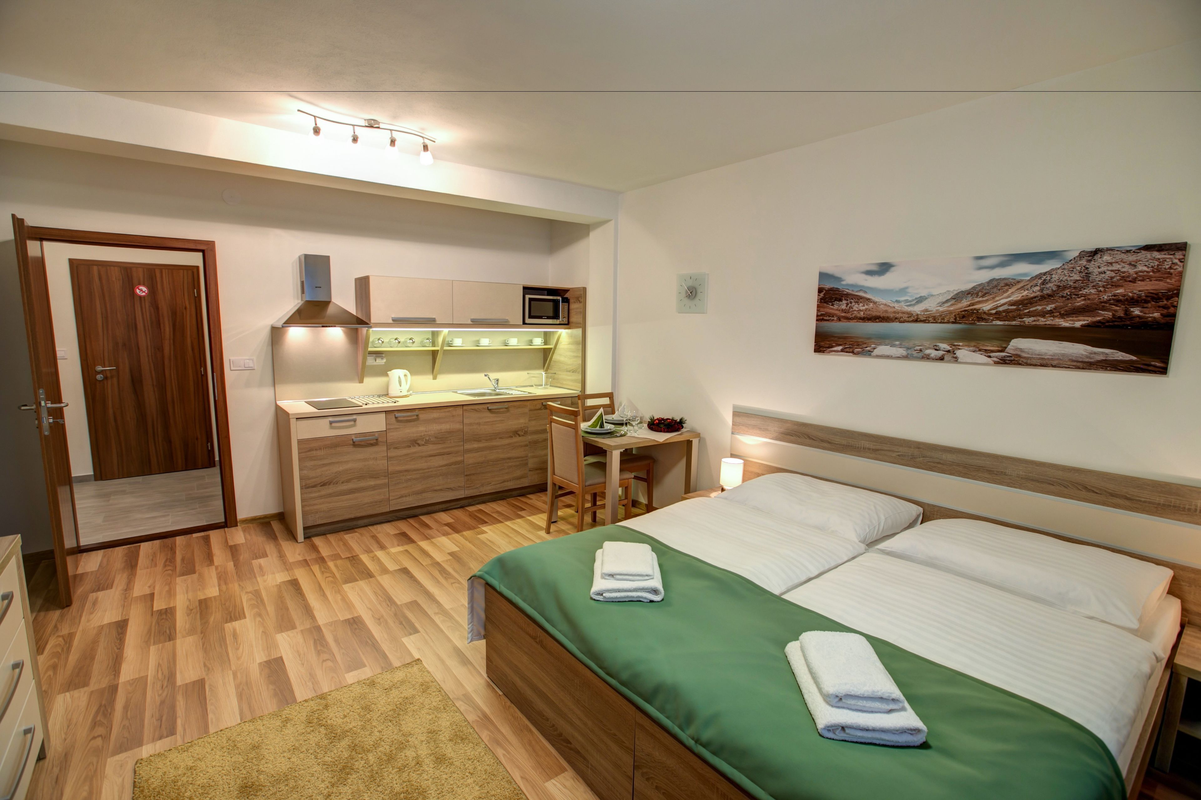 A hotel room with a bed, a desk, a chair, a microwave, a sink, and a door.