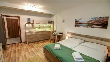 A hotel room with a bed, a desk, a chair, a microwave, a sink, and a door.