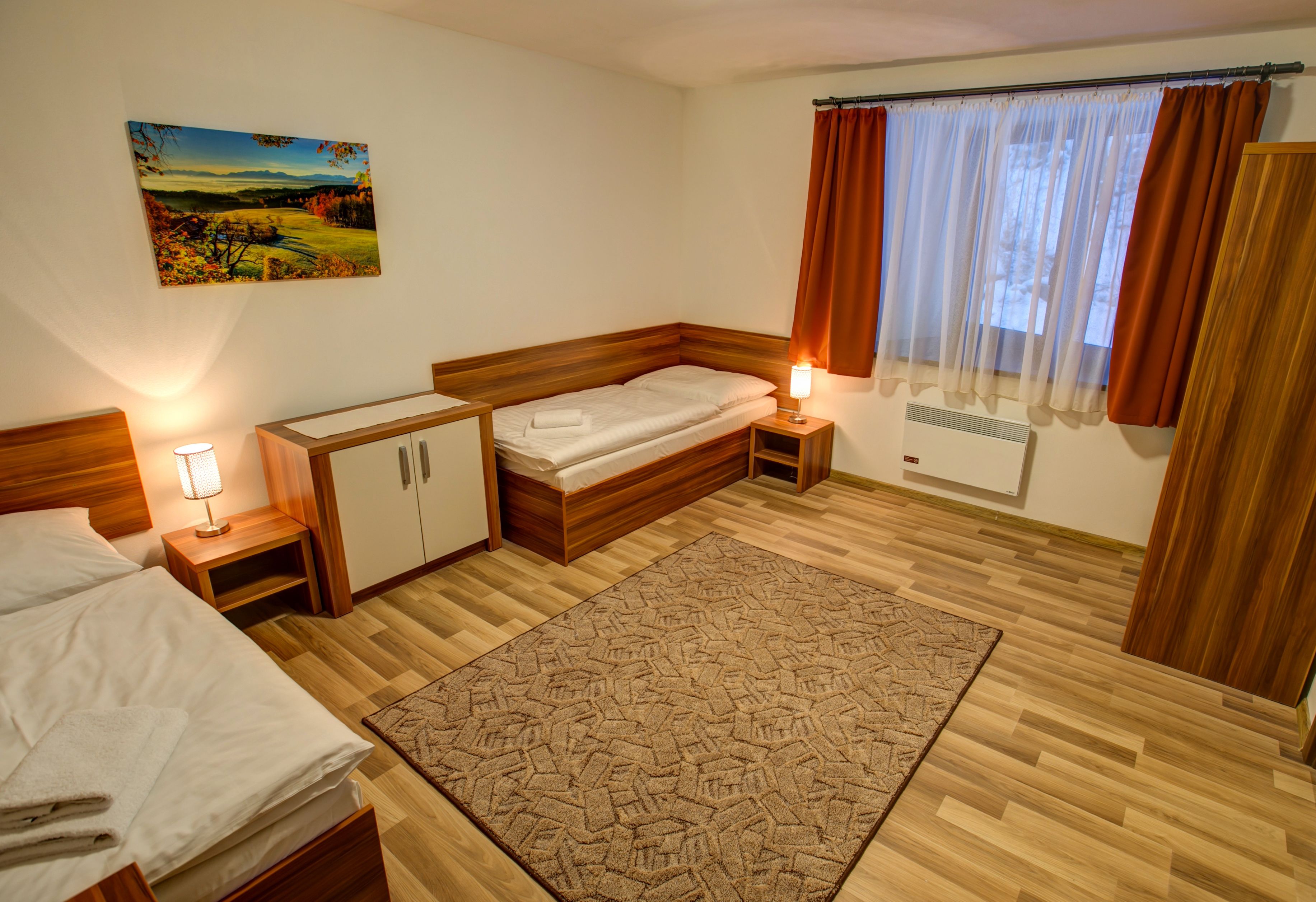 A bedroom with a bed, bedside tables, a nightstand, a rug, a painting, and a window with curtains.