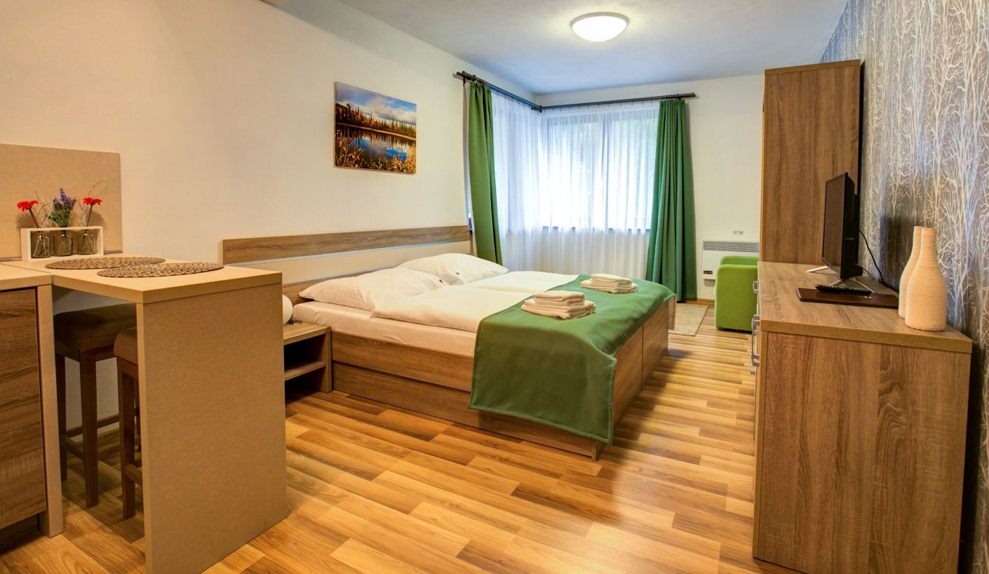 A hotel room with a bed, a desk, a chair, a TV, and a window with curtains.