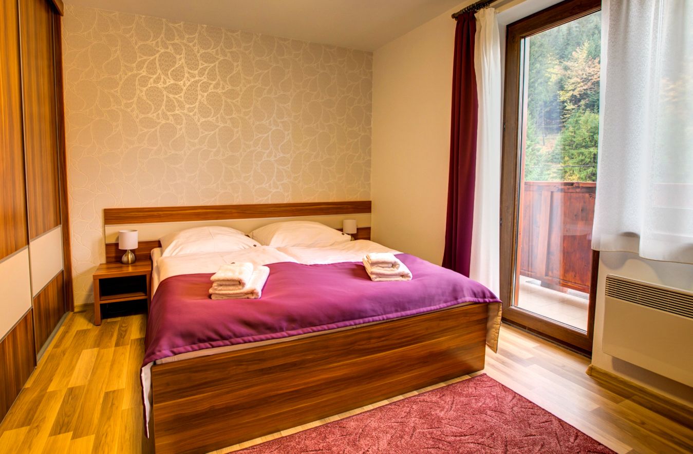A neatly made bed with a purple blanket, a wooden headboard, and a nightstand with a lamp.