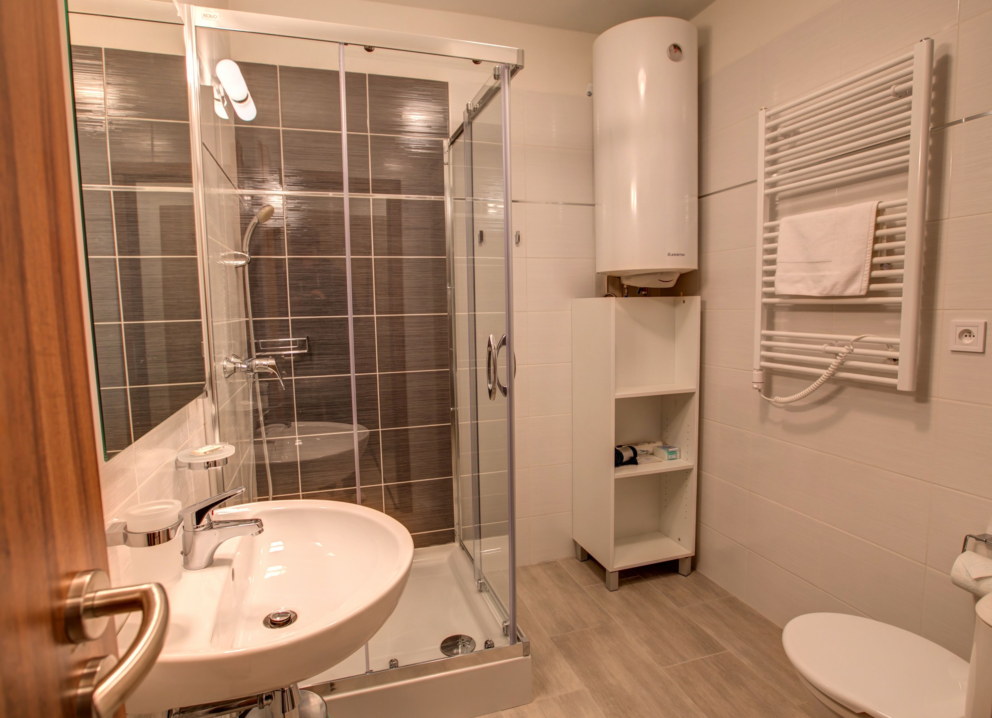 Un baño moderno con ducha envuelta en vidrio, un lavamanos blanco, un inodoro y un perchero para toallas.