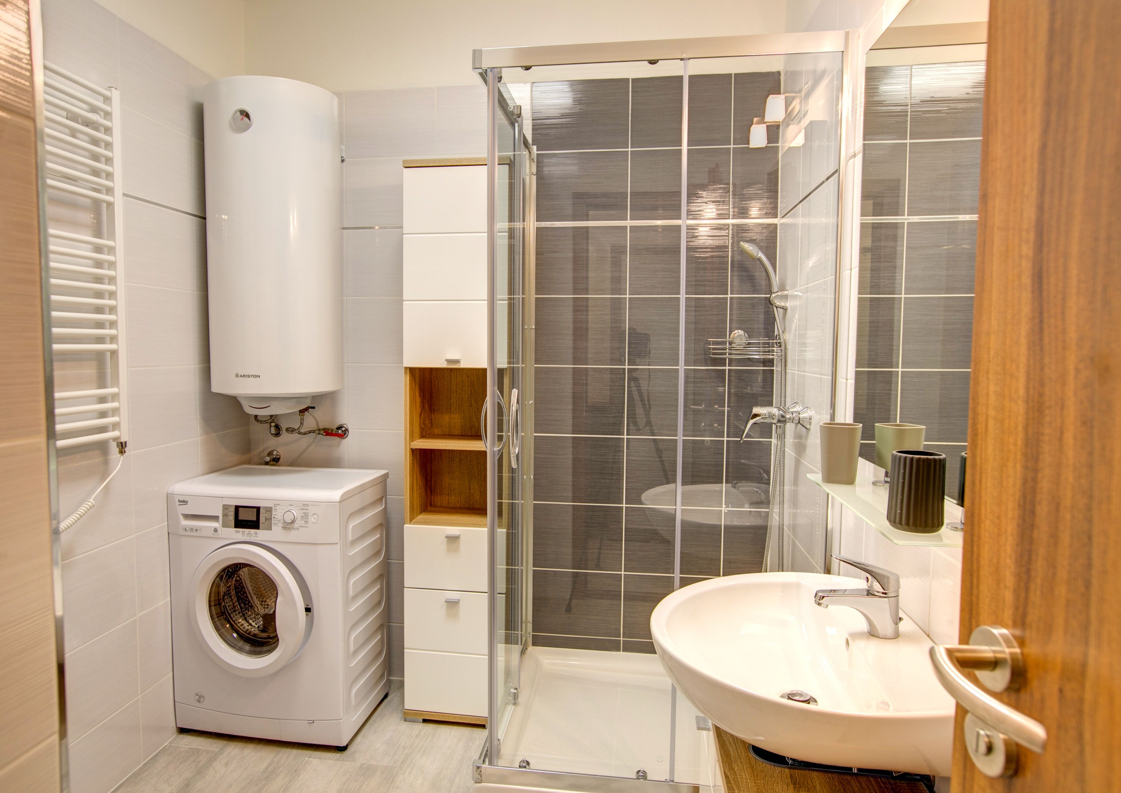A compact bathroom with a built-in washing machine, a glass shower enclosure, and a sink with a mirror.