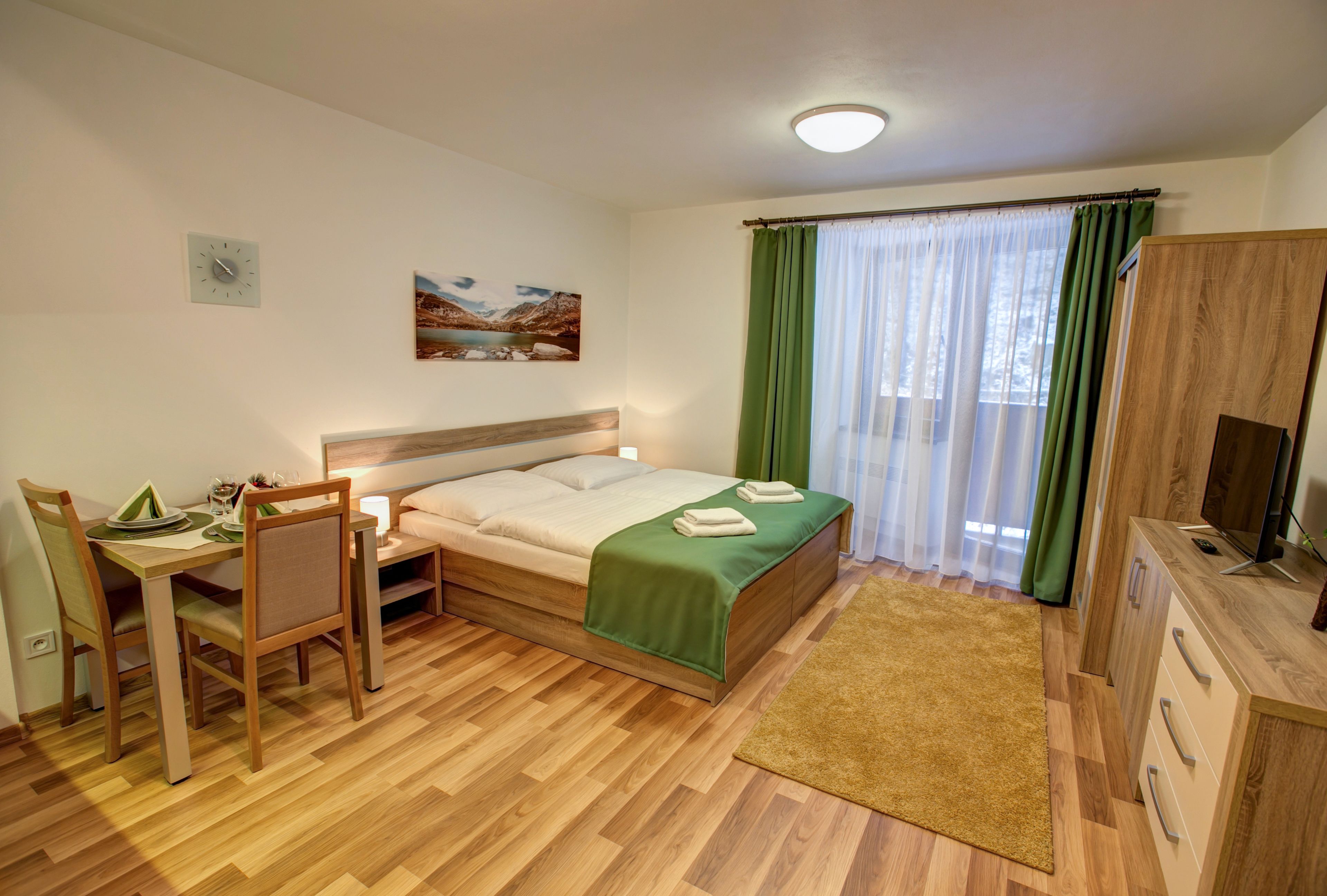 Una camera da letto con un letto, una scrivania con sedie, una TV e un quadro appeso al muro.