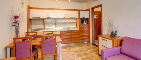 A compact kitchen with wooden cabinets, a dining table with chairs, a microwave, and a small cabinet.