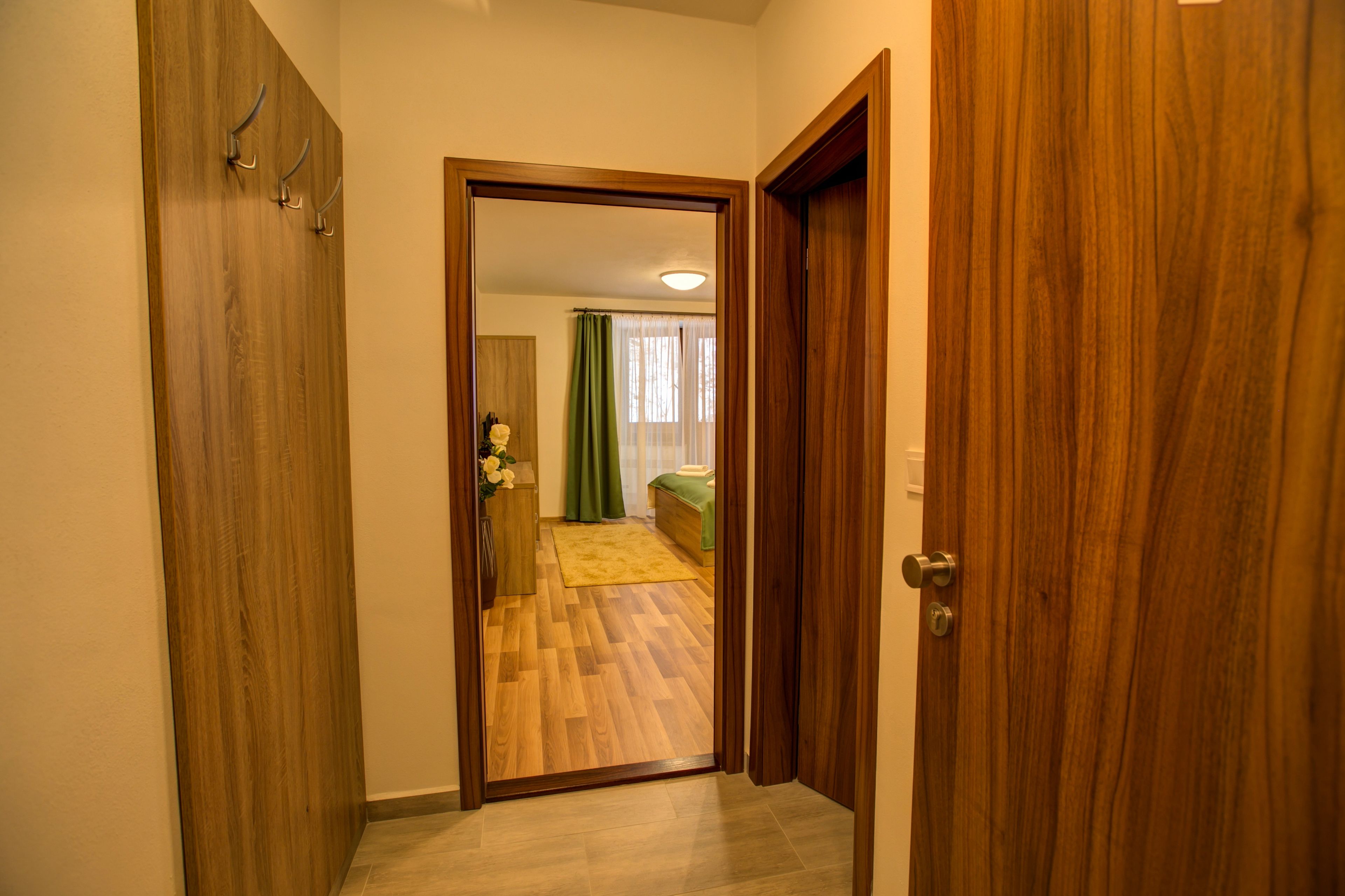 Un pasillo que conduce a un dormitorio con suelo de madera, una cama y una cortina verde.