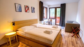 A hotel room with a wooden bed, a small table, a chair, and a desk. - Apartmány TRI STUDNIČKY (Demanovska Dolina)