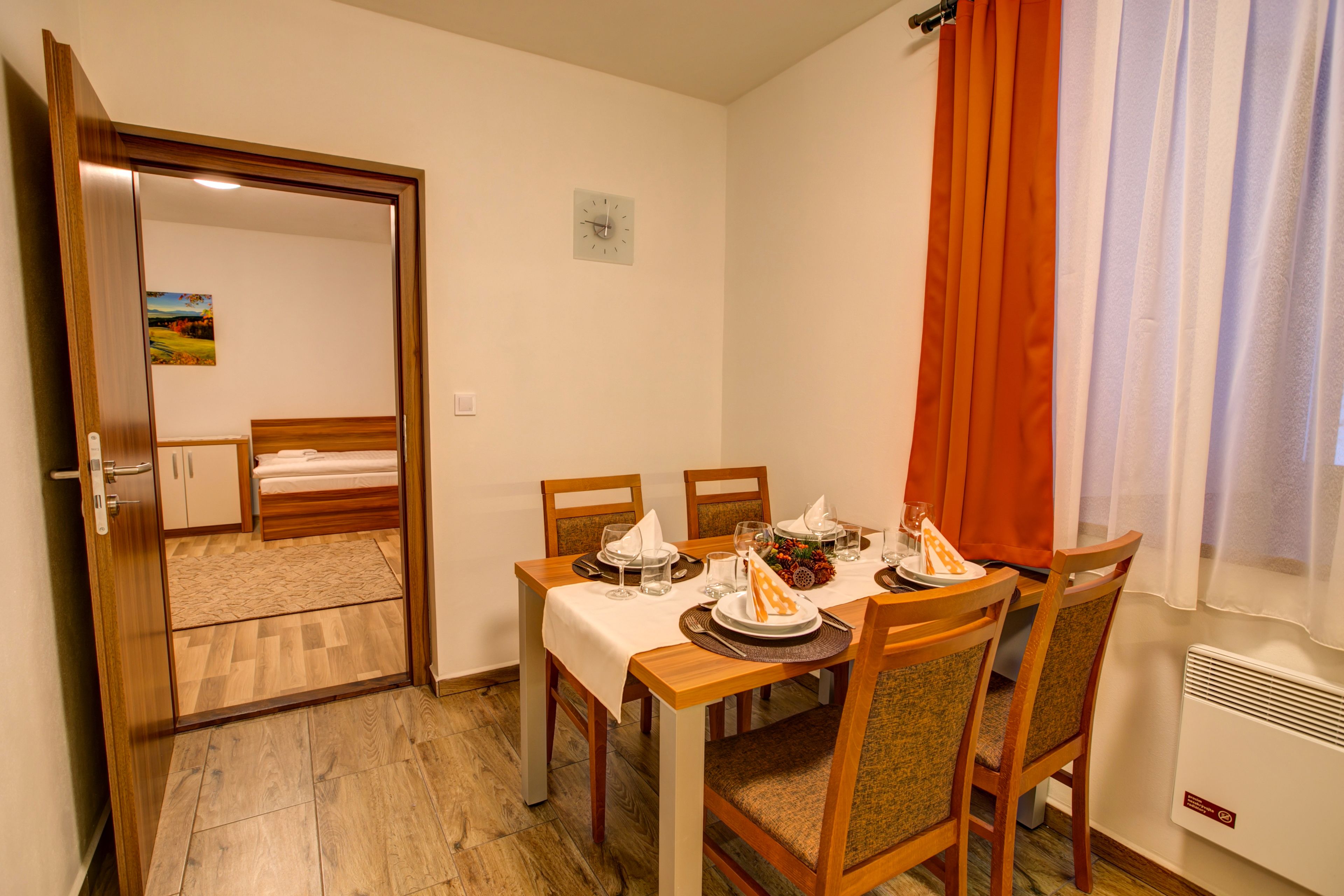 Una habitación compacta con una mesa de comedor dispuesta para cuatro personas, una cama y un pequeño ventanal con cortinas.